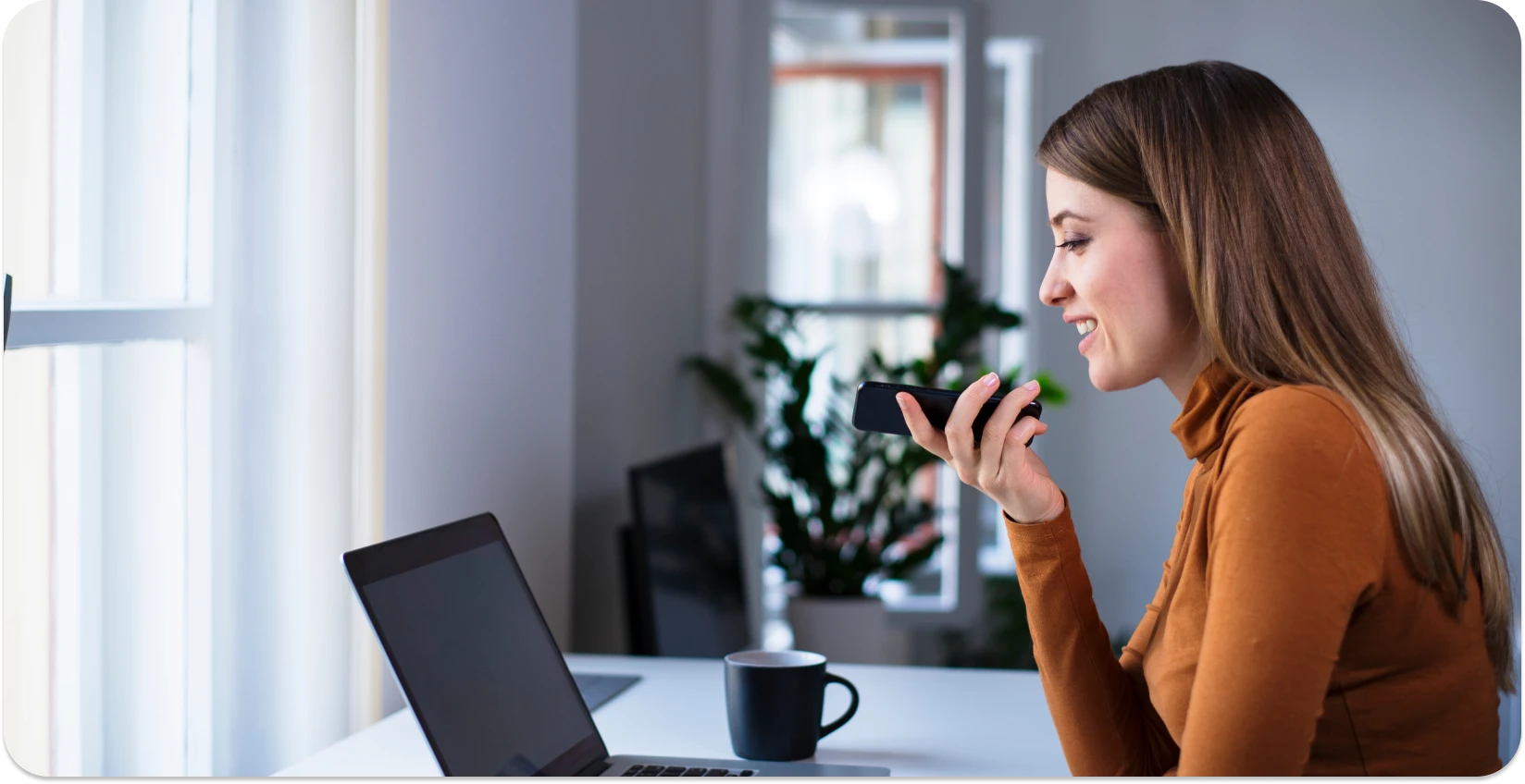 Woman transcribing voice memos on iPhone with a laptop at hand.